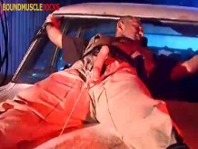 Policía musculoso atado en el coche con la polla afuera