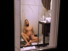 Tío maduro filmado desde afuera mientras se ducha y masturba su polla dura